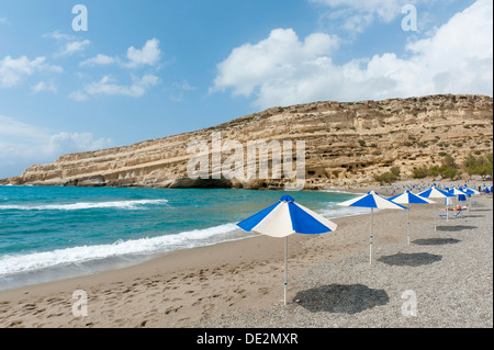 Grotta neolitica abitazioni in pietra arenaria gialla, ombrelloni sulla spiaggia di Matala, ex sito dell'hippies, Creta, Mar Libico Foto Stock