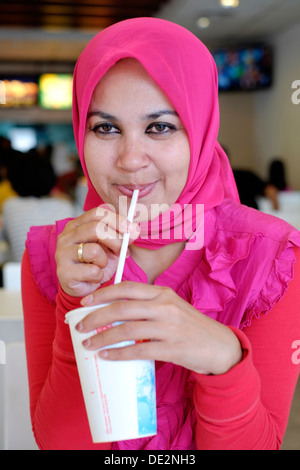 Locale musulmano indonesiano femmina indossando il tradizionale copricapo gustando un drink in un ristorante fast food Foto Stock