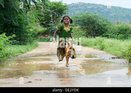 Rurale villaggio indiano Ragazza che corre attraverso una pozza di fango. Andhra Pradesh, India Foto Stock