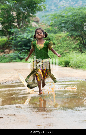 Rurale villaggio indiano Ragazza che corre attraverso una pozza di fango. Andhra Pradesh, India Foto Stock