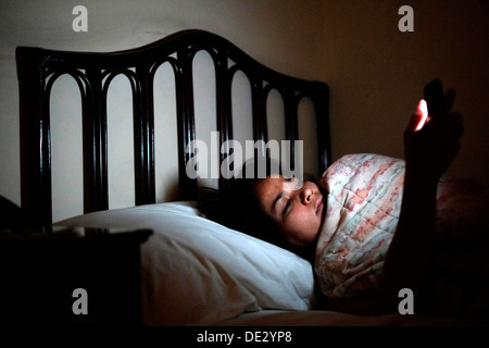 La donna a letto a notte il controllo sociale dei media sul suo telefono mobile Foto Stock