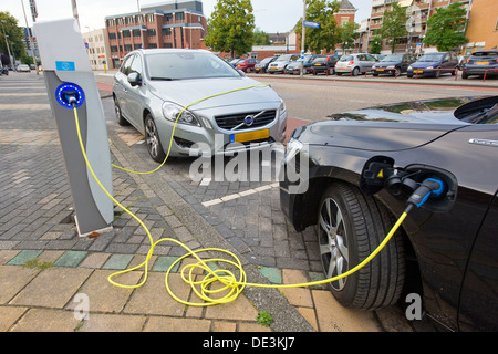 Due le auto elettriche sono parcheggiati in un posto di parcheggio nel centro di una città mentre vengono ricaricati in corrispondenza di una stazione di alimentazione. Foto Stock