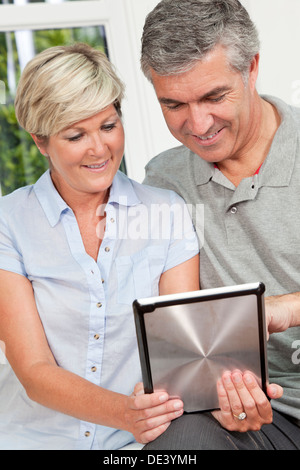 Successo e felice medio di età compresa tra un uomo e una donna matura in loro degli anni quaranta, seduti insieme a casa su un divano utilizzando computer tablet Foto Stock
