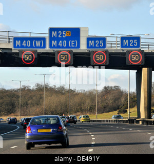 Gli automobilisti che passano sotto i segnali di limite di velocità variabile sul gantry sospeso illuminato sulla strada autostradale M25 UK vicino allo svincolo con M40 London England UK Foto Stock