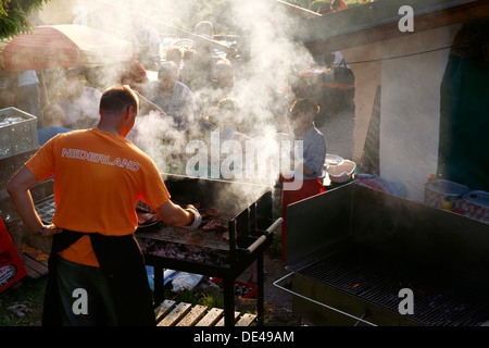 Uomo che indossa un Orange Netherlands shirt la cottura della carne su un barbecue, Chiemgau Alta Baviera Germania Foto Stock