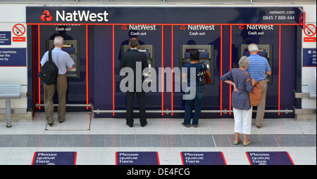 Vista posteriore delle persone che utilizzano o aspettano in tutti e quattro i bancomat di prelievo di contante della Nat West Bank buco nelle macchine a muro all'interno della stazione ferroviaria di Londra Inghilterra Regno Unito Foto Stock