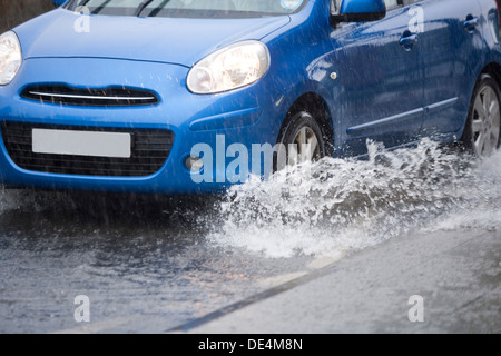 Blue car guida attraverso strade allagate. Foto Stock