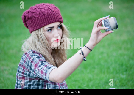 La bionda ragazza adolescente seduto fuori prendendo un autoritratto sul suo telefono. Foto Stock