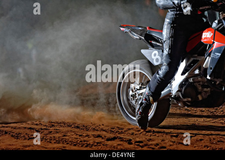 Una pista di motocross moto ruota posteriore la filatura in loco in una pista di sabbia sollevando una nuvola di polvere. Foto Stock