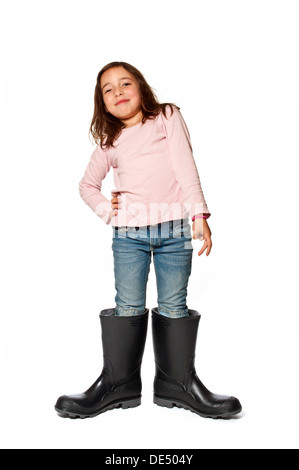 Bambina di sette anni che indossa gumboots che sono di gran lunga troppo grande Foto Stock