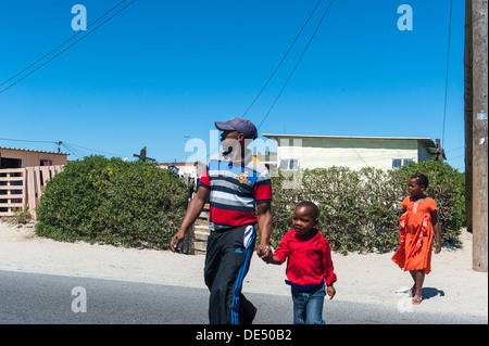 Padre e figli attraversare una strada a Khayelitsha, un informale parzialmente township di Cape Town, Western Cape, Sud Africa Foto Stock