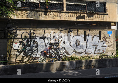 Un negozio di biciclette proprietario in Rothschild Boulevard, Tel Aviv, Israele è la rimozione di una bicicletta da una parete coperta di graffiti Foto Stock