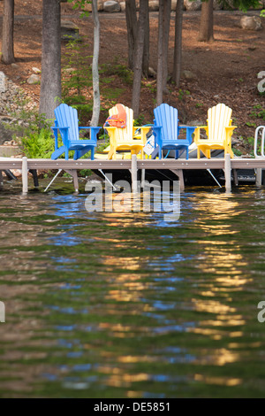 Colorate sedie Muskoka sedersi sul cottage dock con un giubbotto di salvataggio espulso oltre una in attesa di azione Foto Stock