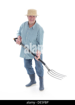 Senior giardiniere donna indossa cappello di paglia e stivali di gomma in posa con forche su sfondo bianco Foto Stock
