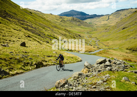 Ciclista salendo la ripida lato ovest di Wrynose Pass nel Lake District inglese con Harter cadde dietro Foto Stock