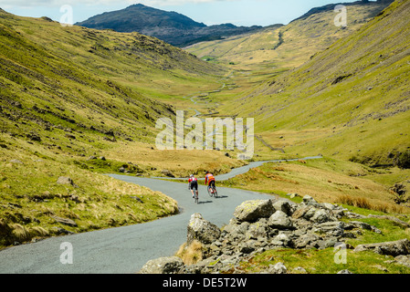 I ciclisti scendono ripidi lato ovest di Wrynose Pass nel Lake District inglese con Harter cadde dietro Foto Stock