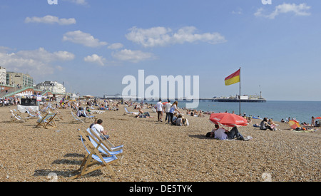 La gente a prendere il sole sulla spiaggia con Pier Brighton East Sussex England Foto Stock