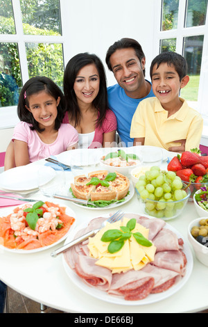 Felice, sorridente Asian famiglia indiana di madre, padre e figlio e figlia di mangiare cibo sano e insalata in un tavolo da pranzo Foto Stock