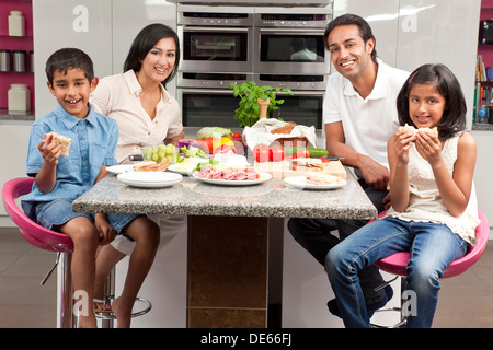 Felice, sorridente Asian famiglia indiana di madre, padre e figlio e figlia di mangiare cibo sano e insalata in cucina a casa Foto Stock
