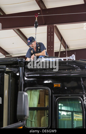 L'uomo allacciato al tettuccio di cablaggio di sicurezza lavorando sul tetto di un camper nella struttura di riparazione. Foto Stock