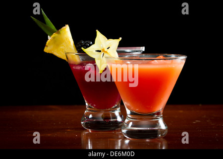 I cocktail serviti in stemless bicchieri da martini guarnito con una fetta di ananas, more e star fruit Foto Stock