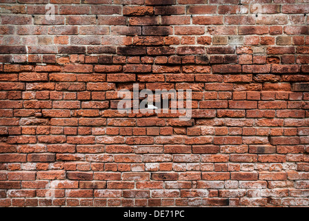 Rosso vecchio muro di mattoni con un mattone mancante nel mezzo. Foto Stock