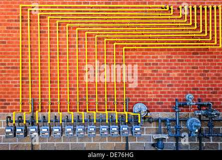 Fila di gas naturale metri con tubazioni gialle sulla costruzione di un muro di mattoni Foto Stock