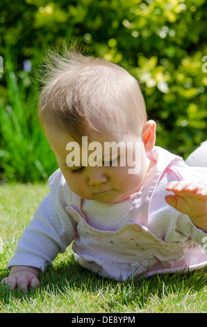 Otto mesi di età bambina fuori in giardino a giocare sull'erba Foto Stock