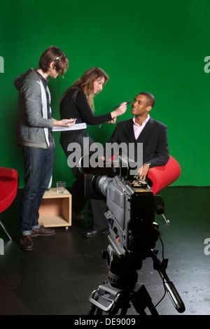 Messa a fuoco selettiva su un studio telecamera con un pavimento manager, make-up artist e presenter fuori fuoco in background. Foto Stock