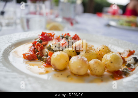 Spigola con pila di pomodori e capperi in italiano al di fuori di una zona pranzo Foto Stock