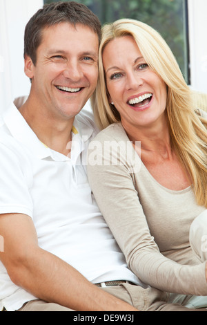 Interessante il successo di una felice uomo di mezza età & donna giovane nella loro degli anni quaranta, seduti insieme a casa sul divano, sorridente ridere Foto Stock