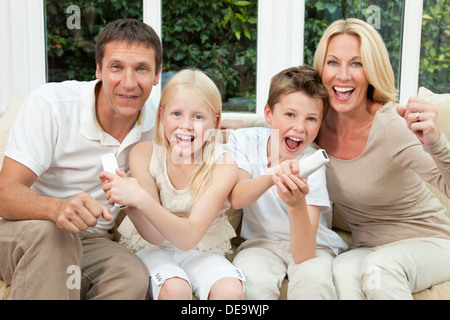 La famiglia felice i genitori, figlio figlia divertendosi console video gioco insieme i bambini hanno i comandi remoti i genitori tifo Foto Stock