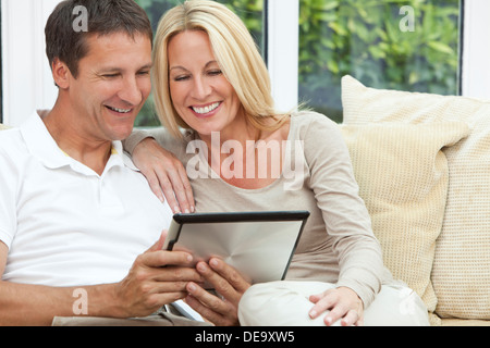 Felice medio di età compresa tra un uomo e una donna matura in loro degli anni quaranta, seduti insieme a casa su un divano utilizzando computer tablet Foto Stock