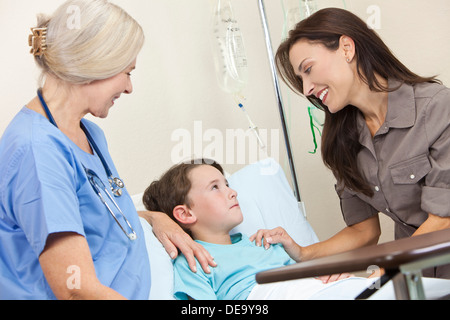 Ragazzo giovane bambino nel letto di un ospedale con sua madre la visita ed un senior donna medico donna Foto Stock