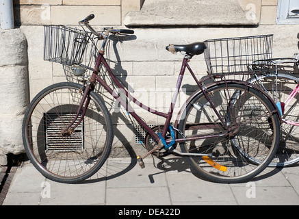 Una vecchia bicicletta appoggiata contro un muro di pietra con cesti Foto Stock