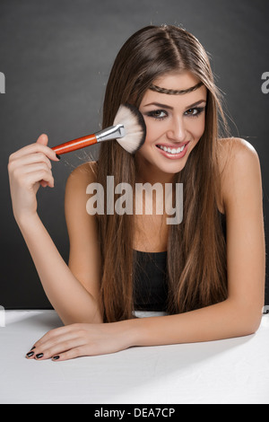 Ritratto di un felice giovane donna di applicare il trucco sul viso con un pennello grande su sfondo scuro. Foto Stock