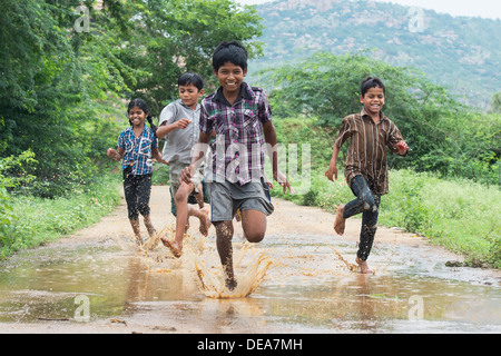 Rurale villaggio indiano i bambini in esecuzione attraverso una pozza di fango. Andhra Pradesh, India Foto Stock