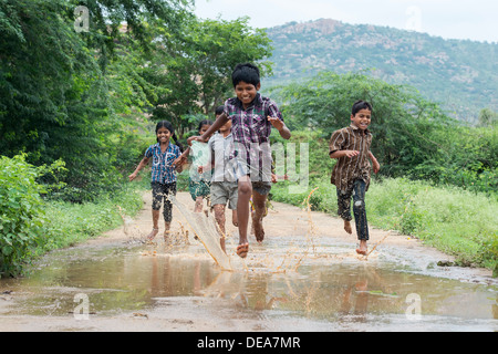 Rurale villaggio indiano i bambini in esecuzione attraverso una pozza di fango. Andhra Pradesh, India Foto Stock