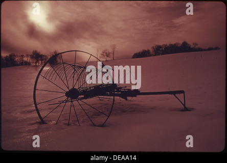 Un rastrello di fieno vecchio stile, un tempo trainato da potenti squadre di cavalli, ora è inutilizzato in un pascolo durante i mesi invernali. Il rastrello di fieno rappresenta la storia agricola e le pratiche agricole tradizionali. Foto Stock