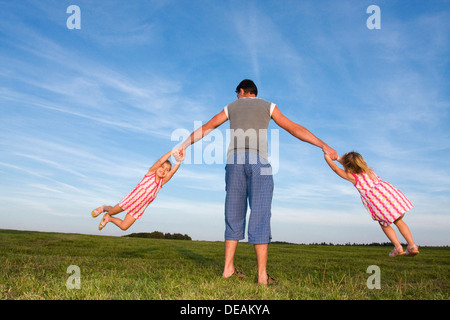 Due gemelle, 3 anni, giocando con il loro padre, 29 anni, all'aperto Foto Stock