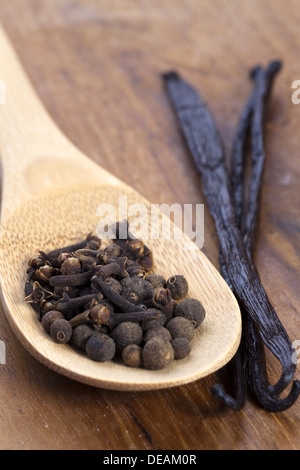 I chiodi di garofano e il pimento spezie su un cucchiaio di legno con baccelli di vaniglia accanto che Foto Stock