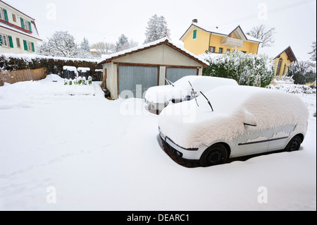 Scena di neve. Due automobili parcheggiate essendo coperte da neve. Essi non sono in garage (in background) Foto Stock