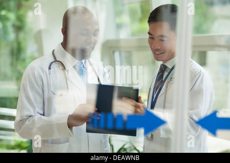 Due medici consulting su medical record sull'altro lato delle porte in vetro Foto Stock