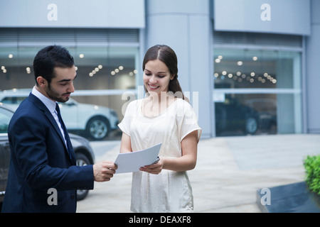 Venditore auto e la giovane donna guardando sopra la documentazione presso una concessionaria auto Foto Stock