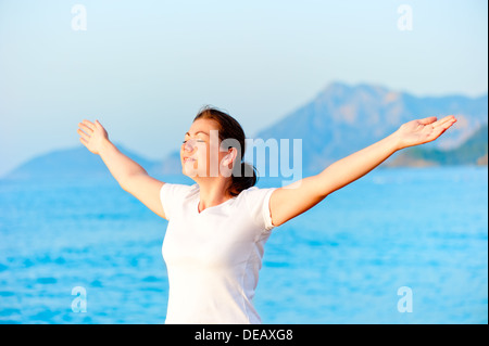Donna con le braccia aperte per godersi il sole in riva al mare Foto Stock