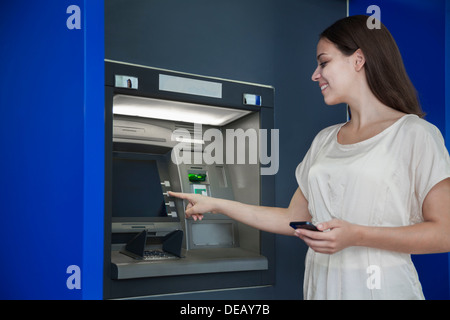 Sorridente giovane donna prelevare denaro dal bancomat Foto Stock