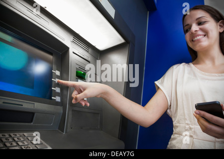 Sorridente giovane donna prelevare denaro dal bancomat Foto Stock