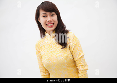 Ritratto di sorridente giovane donna che indossa un giallo abito tradizionale dal Vietnam, studio shot Foto Stock