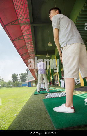 Giovane uomo basculante e colpire palline da golf sul campo da golf Foto Stock