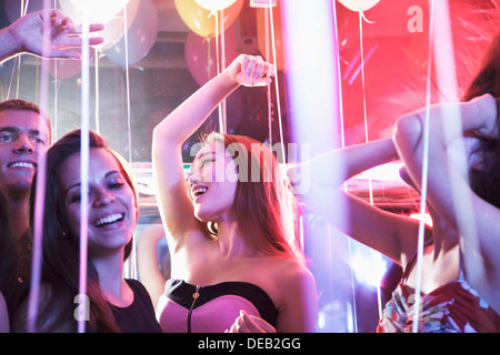 Multi-etnico gruppo di amici con le mani in aria ballando tra i palloncini in un night club Foto Stock